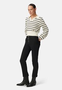 Sweter w paski z dekoltem w serek i ozdobnymi guziczkami, zestawiony z czarnymi dżinsami z wysokim stanem, zapinanymi na guziki, oraz czarnymi botkami do kostki.