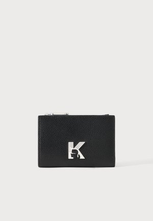 Cartera de cuero negro texturizado con la letra plateada "K" y un pequeño perfil de silueta en la parte frontal, cierre de cremallera en la parte superior.