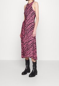 Różowa i czarna w paski sukienka midi z dekoltem halter, gładkiego materiału, o rozkloszowanym kroju, zestawiona z czarnymi botkami za kostkę.