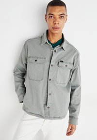 Camisa gris de botones, hecha de algodón, que cuenta con dos bolsillos en el pecho con solapas y un cuello. Textura suave y diseño de corte relajado.