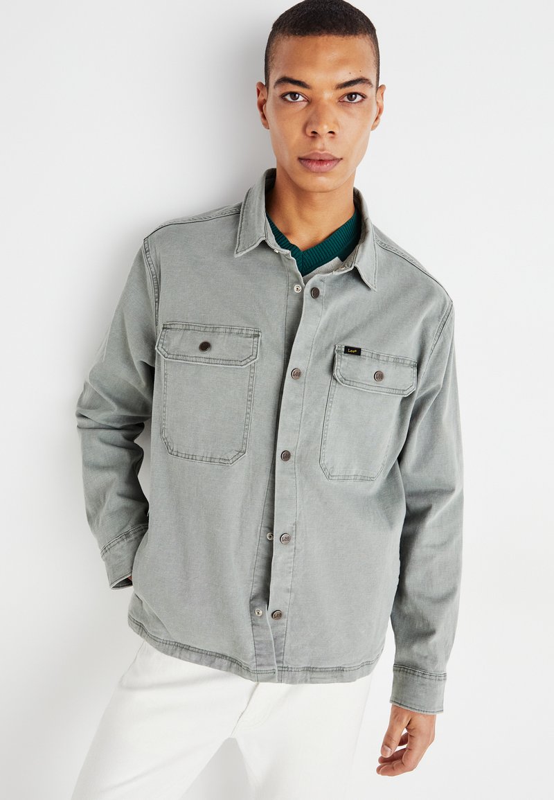 Camisa gris de botones, hecha de algodón, que cuenta con dos bolsillos en el pecho con solapas y un cuello. Textura suave y diseño de corte relajado.