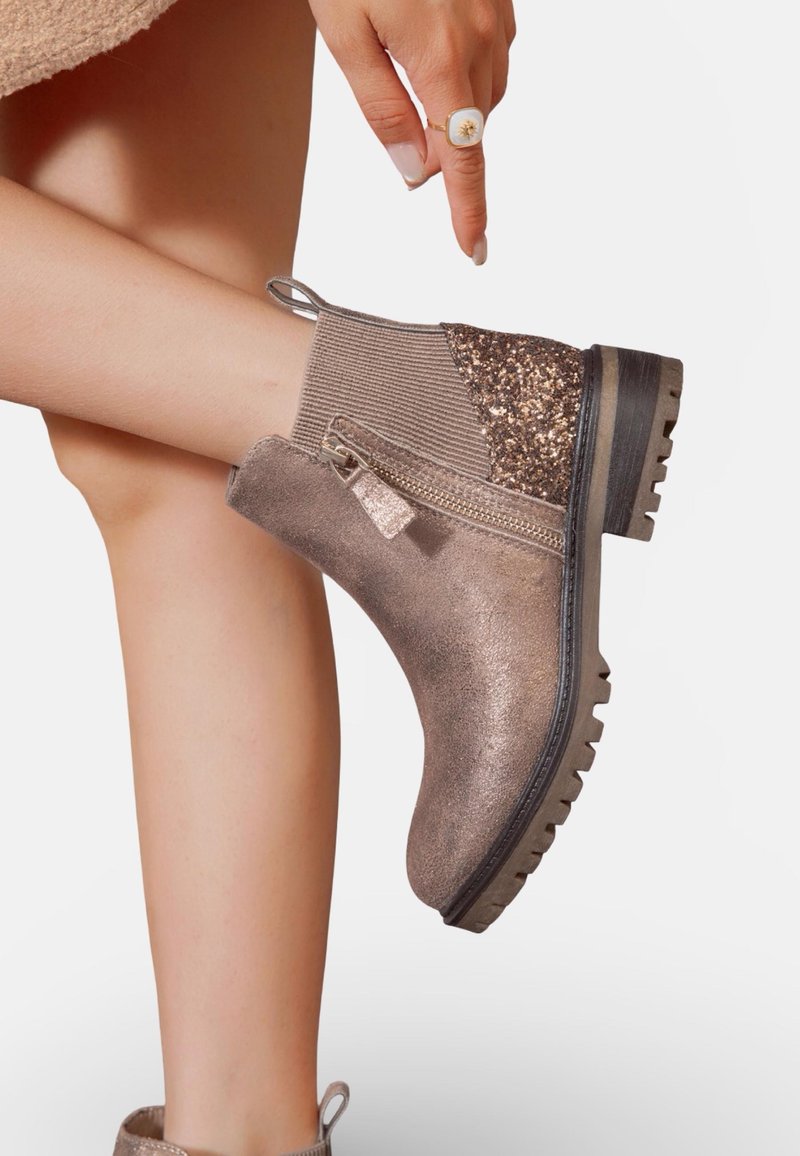 Botte cheville en bronze avec tige texturée, accent scintillant, fermeture éclair sur le côté et semelle robuste. Comprend un détail en maille côtelée et une languette de traction.