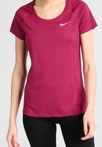 Camiseta deportiva de manga corta Nike en color magenta brillante con una textura suave, con un logo plateado en el pecho izquierdo y un escote redondeado.