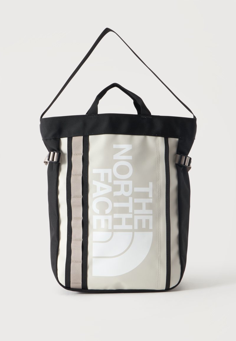 Ορθογώνια μπεζ και μαύρη tote τσάντα North Face με πάνω χερούλια, λουρί ώμου, κάθετο λογότυπο και δύο γκρι κάθετες ρίγες μπροστά.