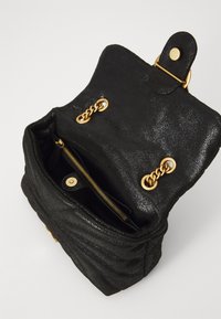 Zwarte handtas met een gestructureerde textuur en een glanzende afwerking, met gouden hardware, een binnenzak met rits en een kettingdetail aan de zijkanten.