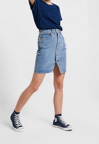 Valkoinen farkkuhame, jossa on etupainike, keskipitkä vyötärö ja halkio. Yhdistetty tummansiniseen t-paitaan ja korkeavartisiin lenkkarit.