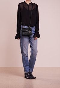 Černá průhledná blůza s řasenými rukávy, zkombinovaná se světle modrými džíny a černými kotníkovými botami na podpatku. Černá crossbody taška s klipem.