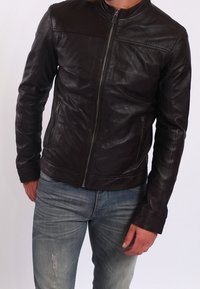 Brun läderjacka med ståkrage, frontdragkedja och två sidofickor. Figursydd design med subtila sömnadsdetaljer.