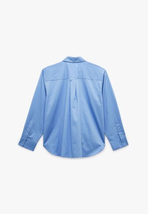 Camisa de manga larga azul claro, fabricada en algodón, con detalle de yugo en la espalda, dobladillo curvado, puños abotonados, textura suave y cuello clásico.