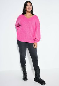 Różowy, oversize'owy sweter dzianinowy z dekoltem w kształcie litery V i bufiastymi rękawami, w połączeniu z czarnymi dopasowanymi dżinsami i czarnymi butami wojskowymi.