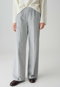 Pantaloni ampi a righe grigie con vita elasticizzata, realizzati in un tessuto morbido. Abbinati a un maglione crema e scarpe scure.