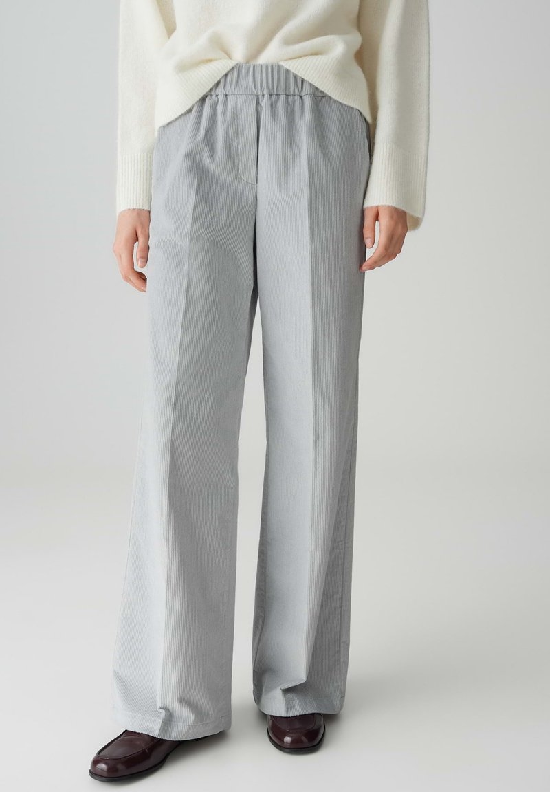 Pantaloni ampi a righe grigie con vita elasticizzata, realizzati in un tessuto morbido. Abbinati a un maglione crema e scarpe scure.