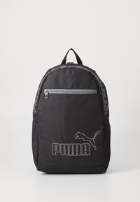 Un sac à dos noir en tissu résistant qui dispose d'une poche zippée à l'avant, d'une poche latérale en mesh et d'accents avec le logo et les lettres blanches de Puma.
