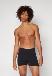 Schwarze Boxershorts aus weichem Material mit einem breiten, elastischen Bund, der ein Logo trägt. Die Passform ist eng und bietet hohen Tragekomfort.