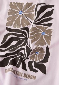 Jasnoróżowa tkanina z kwiatowym wzorem, czarnymi liśćmi, złotymi brokatowymi kwiatami i niebieskimi akcentami w centrum. Tekst brzmi "ŁASKA W PEŁNIM ROZKWIACIE."