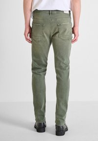 Jeans in denim verde con una vestibilità slim, dotati di due tasche posteriori e vita medio-alta. Il tessuto ha una texture morbida con una leggera scoloritura.
