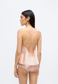 Siidist kampsun pehmes roosas toonis, õhukeste rihmadega, avatud seljaga, komplektis samast materjalist pitsiäärega lühikesed püksid, millel on geomeetrilised mustrid pitsil.