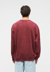 Μπορντό φαρδύ φούτερ με στρογγυλή λαιμόκοψη, μακριά μανίκια και ριμπ μανσέτες. Μαλακό, υφασμένο ύφασμα με ξεθωριασμένο φινίρισμα.