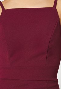 Burgundowa sukienka bez rękawów z dopasowanym gorsetem, teksturowanym materiałem, kwadratowym dekoltem i gładkimi szwami dla uzyskania eleganckiej sylwetki.