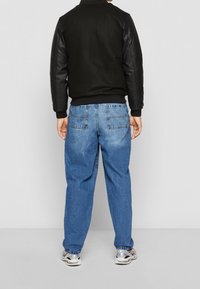 Black bomber jacket with leather sleeves, paired with light blue denim jeans. Sneakers with a gray and white design. Visible back pockets.