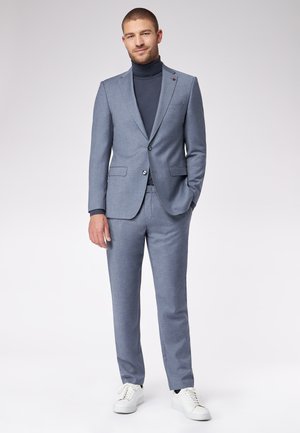 Grijze, op maat gemaakte pak met notch revers, twee knopen en zijzakken, gecombineerd met een donkere coltrui en witte sneakers. Soepele textuur.