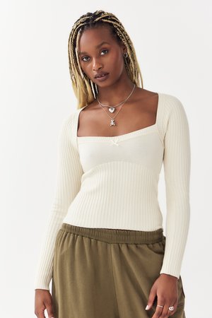 Rippenträgershirt in Creme mit langen Ärmeln und quadratischem Ausschnitt, ausgestattet mit einem zentralen Akzent und einer weichen Textur, kombiniert mit lockeren olivgrünen Hosen.