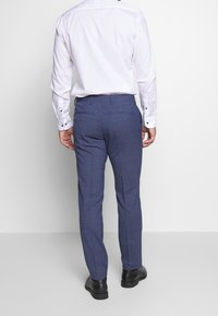 Blue checked trousers made of fabric with a smooth texture, featuring back pockets and a slim-fit design, paired with black shoes.