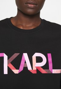 Camiseta de algodón negra con un logo "KARL" de tonos múltiples en formas geométricas rosas, rojas y moradas, y "LAGERFELD" en blanco.