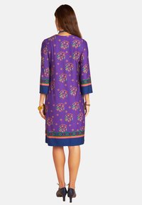 Lila Kleid mit kreisförmigen, mehrfarbigen Mustern, ¾-Ärmeln, blauen Akzenten am Saum und an den Bündchen, glatter Textur, knielanges Design.