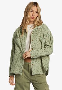 Camisa de pana verde claro con un patrón de leopardo, que cuenta con un cierre de botones, dos bolsillos en el pecho y un ajuste relajado.