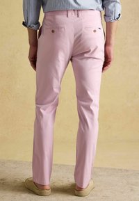 Lichtroze broek met rechte pasvorm, twee achterzakken met gouden details, gecombineerd met een gestreept shirt en casual schoenen.