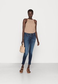 Top de tanque de canalé beige, jeans ajustados azul oscuro, sandalias de dedo al aire color tostado y un pequeño bolso de mimbre; presenta un ajuste relajado y un diseño minimalista.