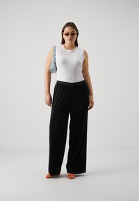 White sleeveless top, black wide-leg pants with ribbed texture, orange sandals, and a light blue handbag. Brown hair, wearing sunglasses.