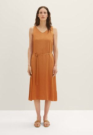 Rooie oranje mouwloze jurk met een V-hals, strik taille detail, gladde textuur en knielengte, gecombineerd met bruine slip-sandalen.