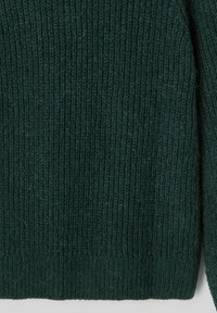 Pull en tricot vert foncé avec une texture côtelée, présentant une finition douce et duveteuse. Le design comprend des manches longues et un col rond.