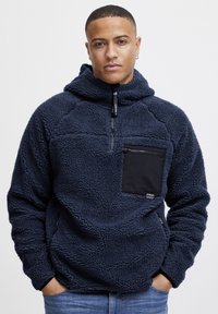 Pullover in pile navy con design a mezza zip. Presenta una tasca sul petto con zip nera, tessuto testurizzato e vestibilità comoda.