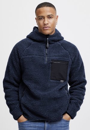 Pull-over en polaire marine avec un design à demi-zip. Présente une poche poitrine zippée noire, un tissu texturé et une coupe décontractée.