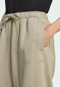 Lysebrune sweatpants med elastisk talje og snor. Har sidelommer og præget Adidas-logo nær kanten. Blød tekstur.
