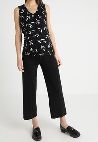 Top sin mangas negro con estampado de hojas blancas, combinado con pantalones cortos negros. Modelo vistiendo mocasines negros brillantes. Diseño simple y moderno.