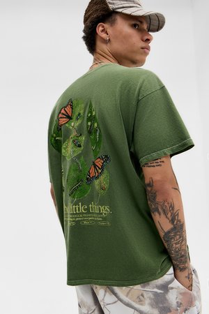 Olivgrünes Baumwoll-T-Shirt mit einem gedruckten Design aus Schmetterlingen und Blättern auf der Rückseite, mit Text darunter. Lockere Passform mit Rundhalsausschnitt.