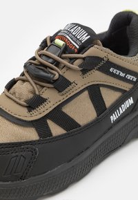 Chaussure imperméable avec un design marron et noir, présentant une tige texturée, un embout renforcé et un système de laçage ajustable.