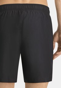 Bañador negro hecho de material ligero con cintura elástica, que presenta una textura suave y un corte de longitud estándar.