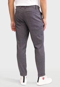 Grijze gepatternde broek met een aansluitende pasvorm, voorzien van zij- en achterzakken. G gedragen met witte sneakers en een plain shirt.