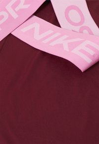 Primer plano de tela burdeos con bandas elásticas rosa claro que muestran parcialmente la palabra "NIKE" y letras circulares.