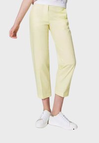 Pantaloni cropped giallo chiaro realizzati in un tessuto liscio, con una vestibilità su misura e tasche laterali, abbinati a sneakers bianche.