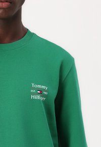 Felpa verde in cotone, con colletto e polsini a costine, dotata di logo ricamato bianco e rosso con la scritta "Tommy Hilfiger EST. 1985."