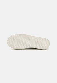 Talpă de pantof din cauciuc alb cu un model texturat. Prezintă un vârf rotunjit și o ușoară curbură pe laturi. Marcată cu numele brandului.