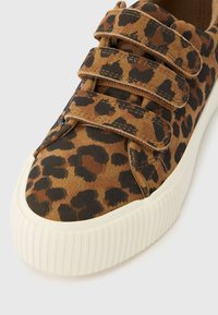 Barnsneaker med leopardmönstrat tyg och tre bruna kardborreband, vit texturerad gummisula, närbild på tåområdet.