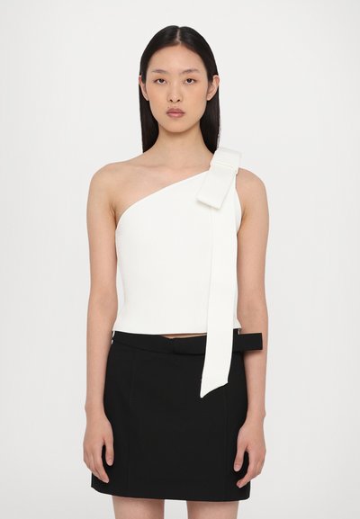 Weißes One-Shoulder-Oberteil mit strukturiertem Finish und kontrastierendem Banddetail; kombiniert mit einem enganliegenden schwarzen Rock mit passendem Gürtel.