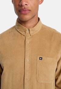 Πουκάμισο από κορδονέ ύφασμα σε ανοιχτό καφέ χρώμα με γιακά με κουμπιά, διαθέτει τσέπη στο στήθος και μικρό λογότυπο πάνω στην τσέπη.